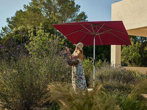 Frau im Garten unter rotem Sonnenschirm Glatz Alu Twist zwischen Pflanzen und moderner Terrasse