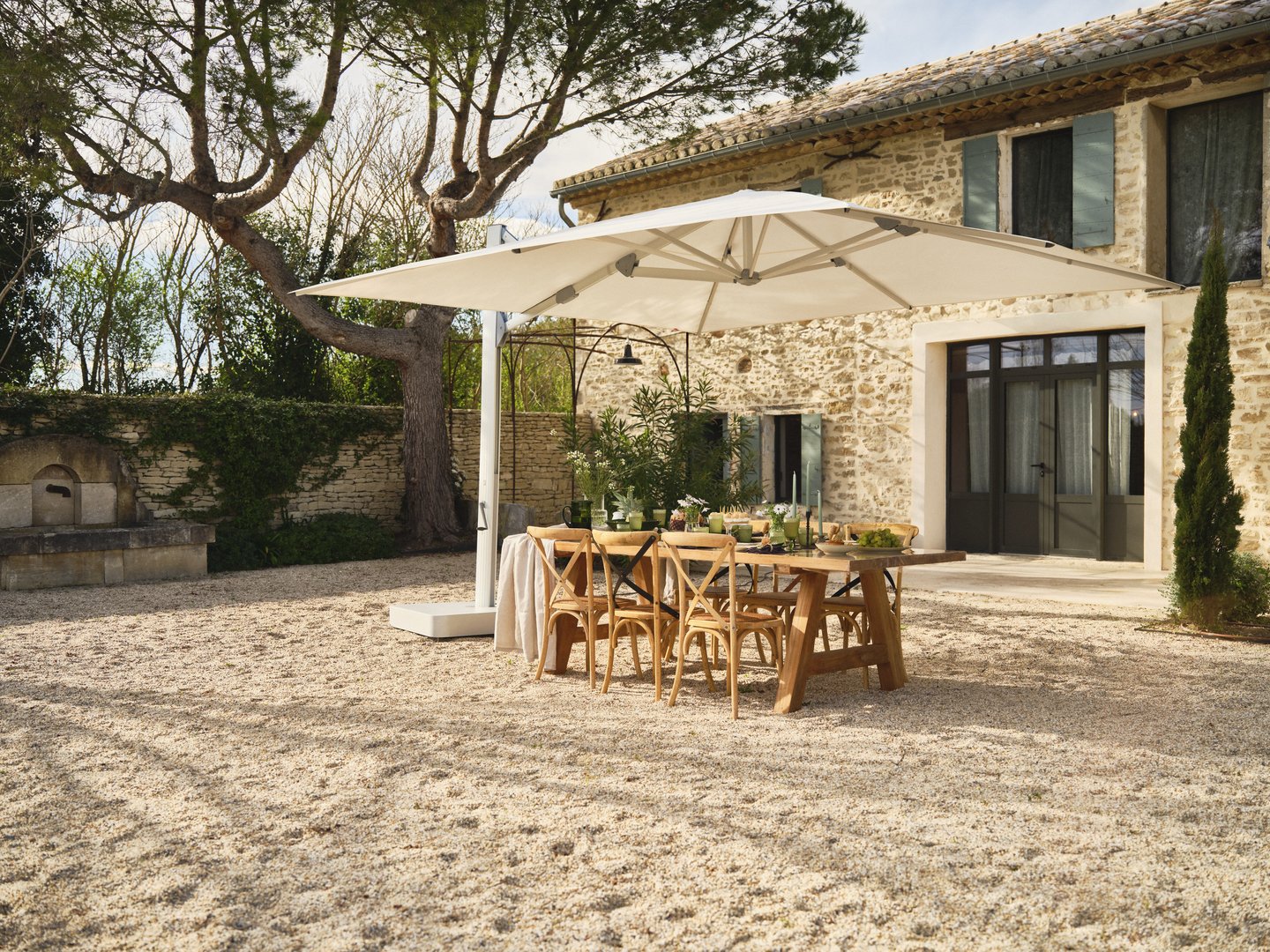 Eleganter Ampelschirm Glatz Ambiente Nova über einem Esstisch im Garten vor einem Natursteinhaus