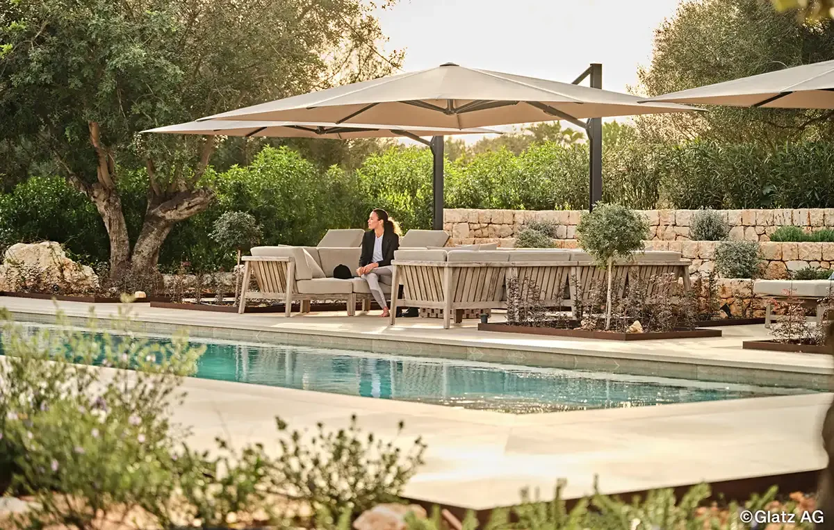 Mehrere große Ampelschirme Glatz Ambiente Nova spenden Schatten auf einer modernen Terrasse mit Pool und Lounge Möbeln