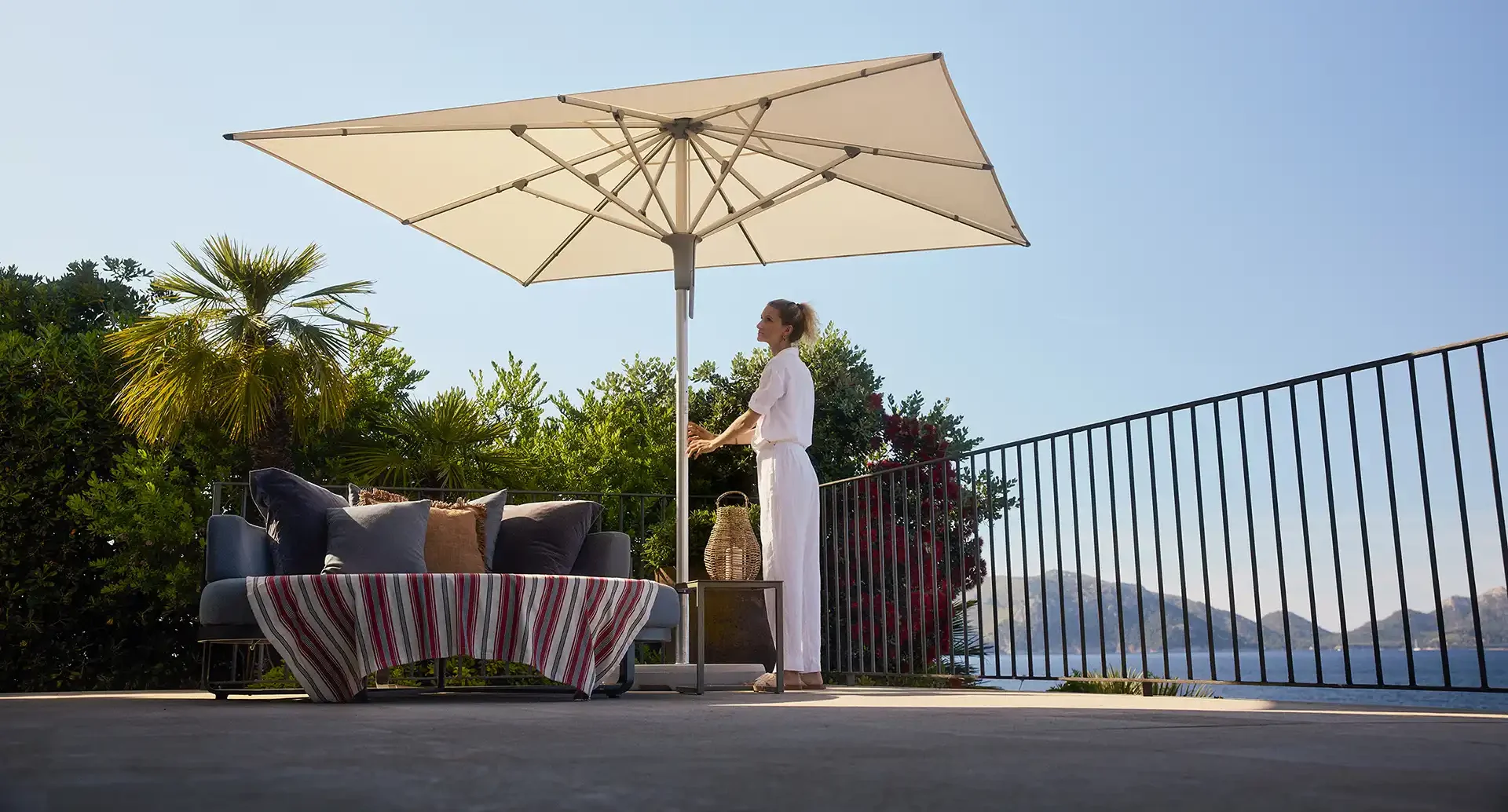 Eine Frau spannt einen beigen Sonnenschirm auf einer Urlaubsterrasse auf